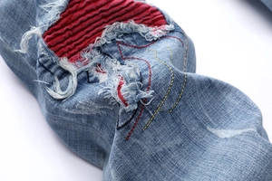 Macro detail of men's distressed light blue jeans with red ribbed fabric and yellow stitching