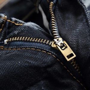Jean droit déchiré pour homme, détail de la fermeture éclair en bronze et texture du denim