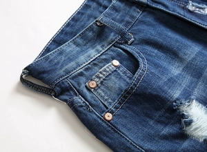 Detail of dark blue denim shorts featuring washed texture, distressed holes, and metal rivets