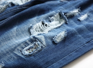 Detail of distressed dark blue denim with heavy frayed holes and multi-color stitching details