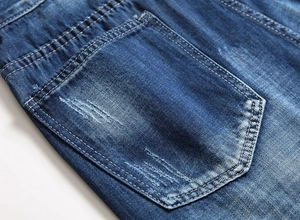 Detailed macro view of distressed blue denim back pocket with hand-made rips and fading
