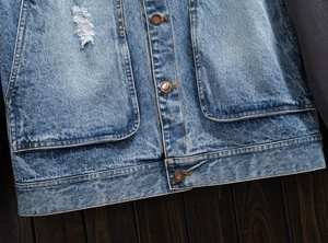Close-up of washed blue denim jacket featuring distressed rips and copper JEANS buttons