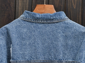 Close-up of the vintage blue denim jacket collar and shoulder stitching on a wooden hanger