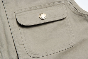 Dettaglio tasca gilet kaki in tessuto twill di cotone con bottone metallico inciso