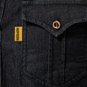 Détail de la poche de chemise en denim noir avec étiquette jaune et bouton en bois