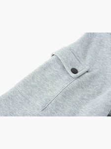 Détail de la poche du sweat gris clair avec bouton pression noir mat et texture coton
