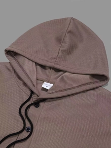 Makro-Detail von braunem Waffel-Hoodie mit Kapuzenkordel und Knöpfen am Halsausschnitt