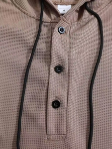 Makroaufnahme von khakifarbenem Waffelstrickstoff mit Knöpfen und Kapuzenkordel am Herren-Hoodie
