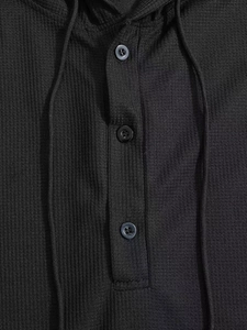 Detailansicht des schwarzen Waffelstrick-Hoodies mit Dreiknopfleiste und Kordelzug-Textur