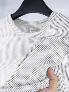 Makroaufnahme eines weißen T-Shirts mit strukturiertem Muster und Größenetikett S am Kragen