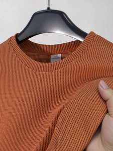 Detail eines gebrannten orangen Strick-T-Shirts mit feiner vertikaler Rippenstruktur