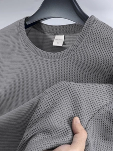 Detailansicht der grauen Waffelstrick-Struktur und des Markenetiketts auf dem Kurzarm-Shirt