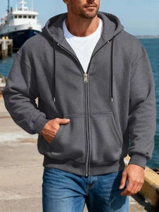 Men's dark grey zip-up hoodie with drawstring and ribbed cuffs in a scenic harbor setting