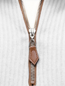 Detailed close-up of silver metal zipper with brown leather puller on white ribbed fabric