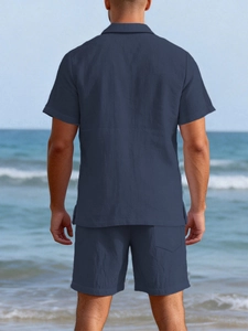 Back view of a men's navy blue linen shirt and shorts set on a beach background