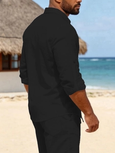 Detail of black linen shirt sleeve with roll-up tab and button on beach background