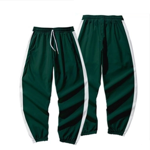 Détail d'un pantalon de jogging vert foncé avec bandes latérales blanches et cordon de serrage