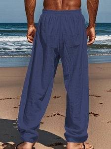 Rear view of men's loose linen pants in navy blue on a scenic summer beach setting