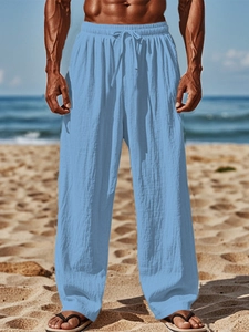 Detail of light blue linen joggers featuring drawstring elastic waist on a beach background
