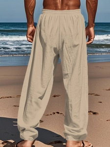 Men's loose linen pants with elastic waist shown from behind on a beach setting