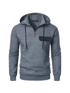 Detail eines grauen gesteppten Hoodies mit Viertelreißverschluss und schwarzer Brusttasche