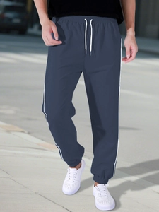 Detail of navy blue parachute joggers with white drawstring and side stripe styling
