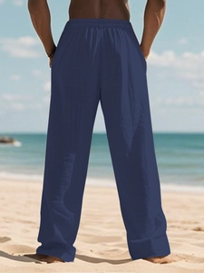 Men's navy blue linen pants featuring a relaxed straight fit and elastic waist on the beach