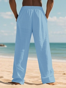 Rear view of men's sky blue linen pants showing the relaxed fit on a sunny beach