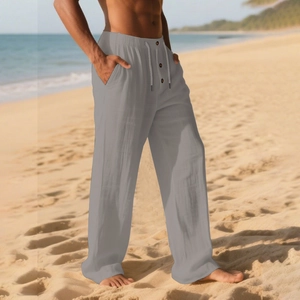 Detail of light gray linen pants with elastic drawstring waist and buttons on a beach