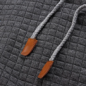 Detail of dark grey waffle quilted hoodie featuring brown leather aglets on drawstrings