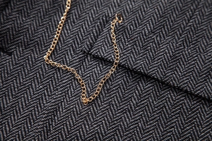 Macro shot of gold metal chain detail on dark grey herringbone fabric vest suit