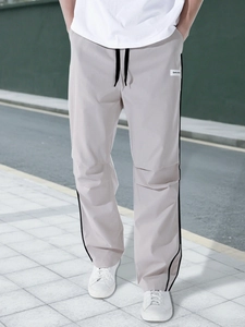 Detailed view of grey parachute pants with black drawstring waist and side stripes