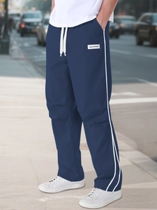 Detail of navy blue parachute pants showing adjustable drawstring waist and side stripes