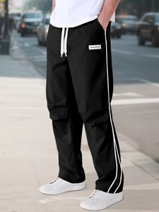 Detail of black sports trousers featuring side stripes, drawstring and logo label