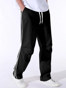 Detail view of black parachute pants featuring side stripes and drawstring waist design