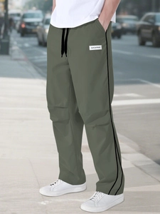 Detail of olive green athletic joggers featuring side black stripes and a woven logo label