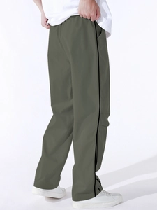 Detail view of olive green parachute pants featuring black side stripes and elastic waist