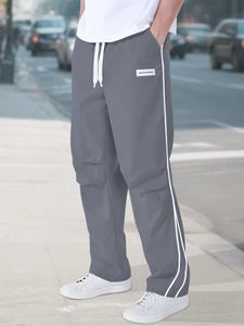 Detail of dark grey parachute pants featuring white side stripes and adjustable drawstring