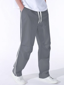 Detail of dark grey parachute pants featuring elastic waist, white drawstrings and side stripes