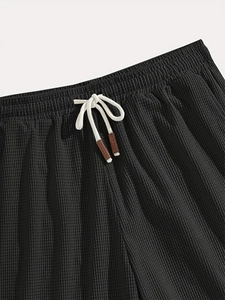 Detail of black waffle knit shorts featuring elastic waistband and white braided drawstrings