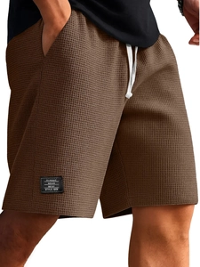 Dettaglio dei pantaloncini in maglia a nido d'ape marrone scuro con coulisse e logo patch