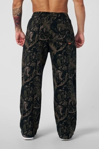 Dettaglio dei pantaloni mimetici larghi con motivo a foglie e etichetta arancione sulla tasca
