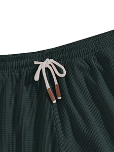Detail of waffle textured shorts with elastic waist and cream drawstrings in dark green