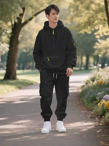 Male model in black hoodie and cargo jogger set with neon yellow zipper accents outdoors