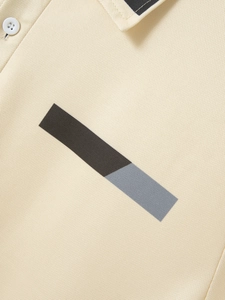 Detail of beige polo shirt showing pique texture, button collar and geometric chest print