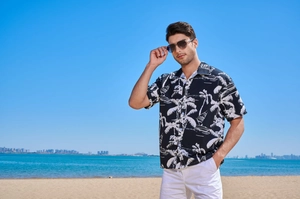 Close-up of men's Hawaiian shirt with tropical white palm tree print on black fabric