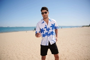 Men's Hawaiian shirt with blue coconut tree print on a white beach background