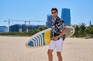 Men's retro Hawaiian floral shirt and white shorts set at beach with surfboard