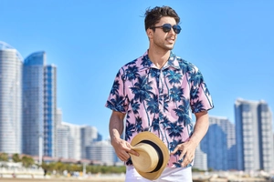 Detail of pink men's Hawaiian short sleeve shirt with navy palm tree prints on beach