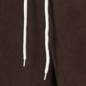 Detailed view of dark brown corduroy texture with white woven drawstrings and plastic tips